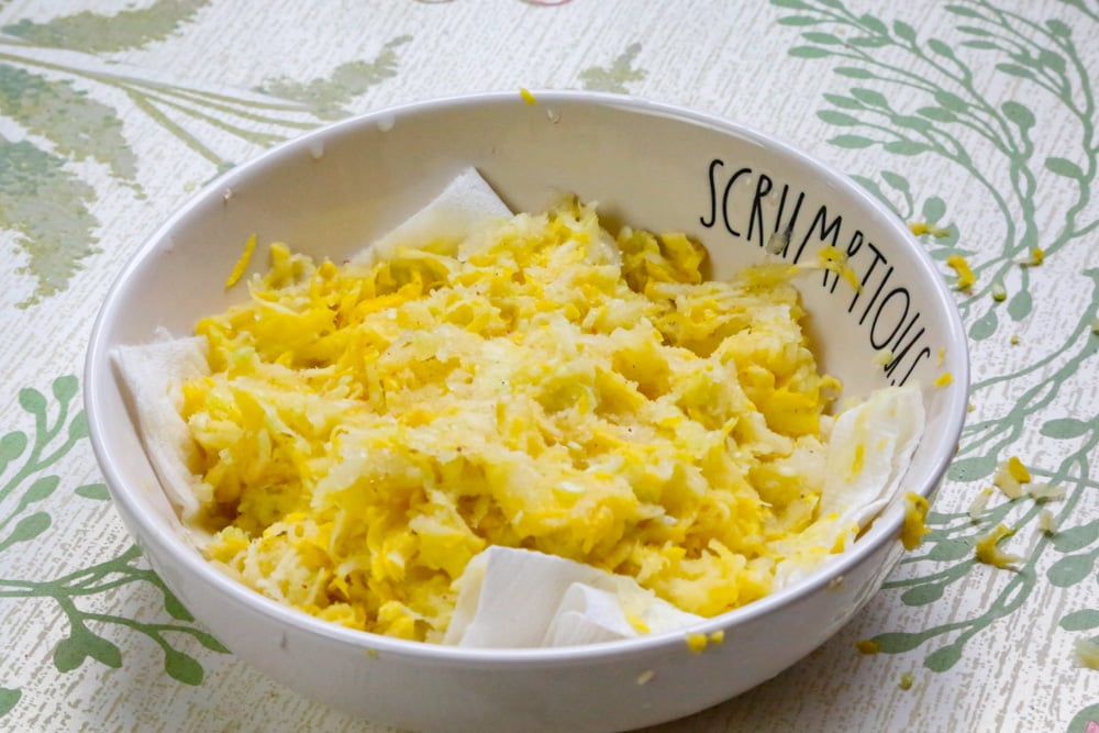 Preparing grated yellow squash for homemade squash fritters by salting and draining excess moisture.