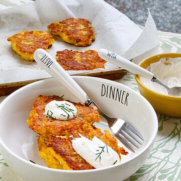 Crispy yellow squash fritters with sour cream and fresh chives served in a white bowl with additional fritters in the background.