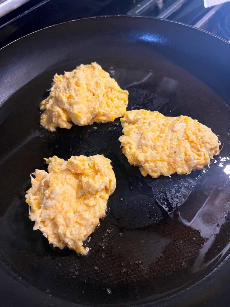 Homemade squash fritter batter formed into patties and cooking in a skillet.
