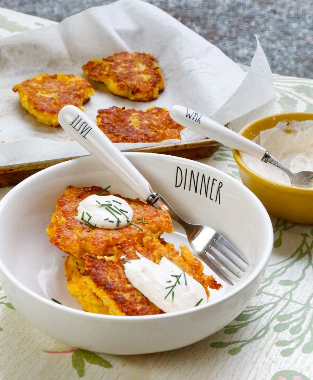 Crispy yellow squash fritters with sour cream and fresh chives served in a white bowl with additional fritters in the background.