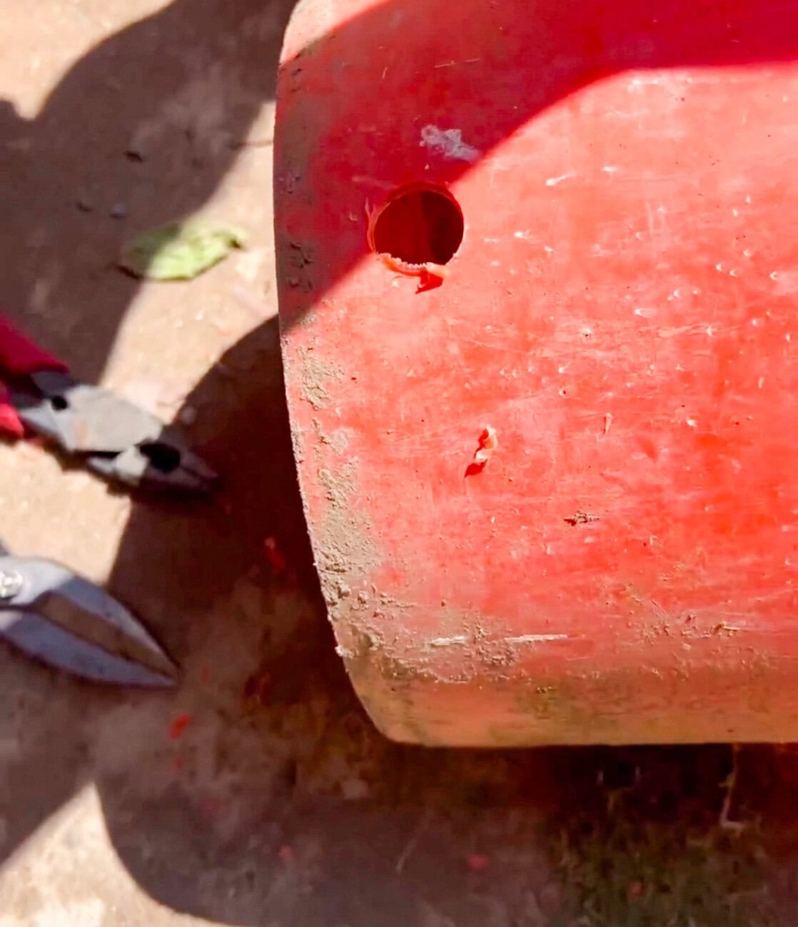 Close-up of a drilled hole in an orange utility bucket for a DIY outdoor hose and extension cord storage project.
