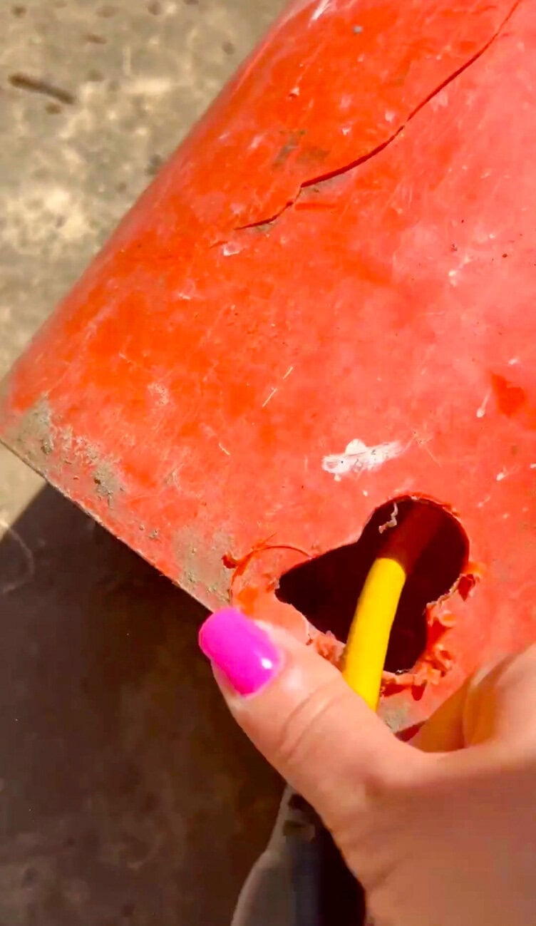 Garden hose being threaded through a drilled opening in an orange utility bucket for a DIY outdoor hose storage hack.
