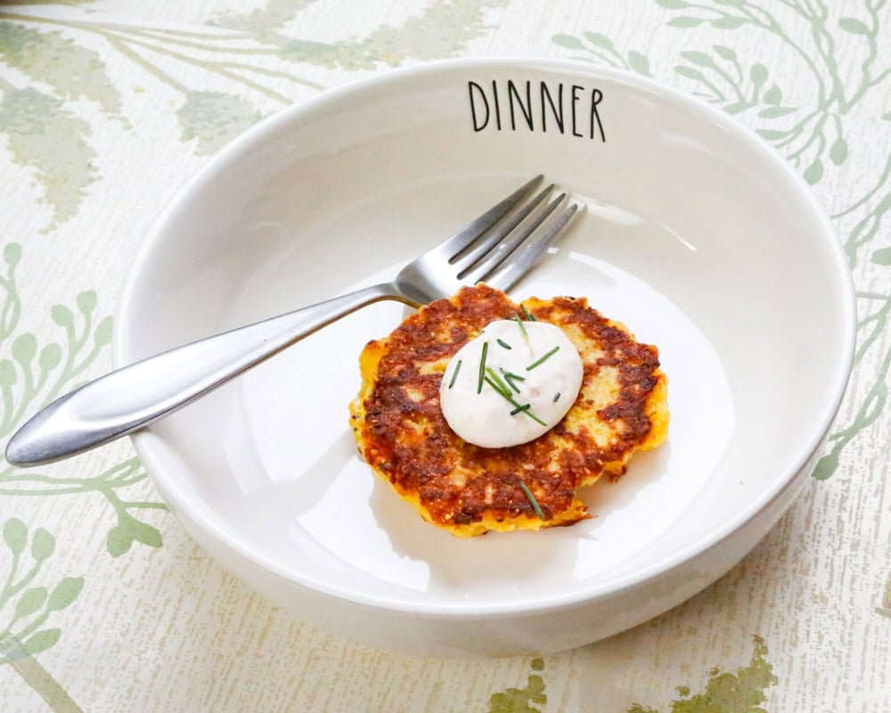 Homemade yellow squash fritter topped with sour cream and fresh chives in a white serving bowl.