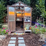 Easy garden path made with stepping stone pavers, mulch, and weed barrier fabric leading to a backyard greenhouse.