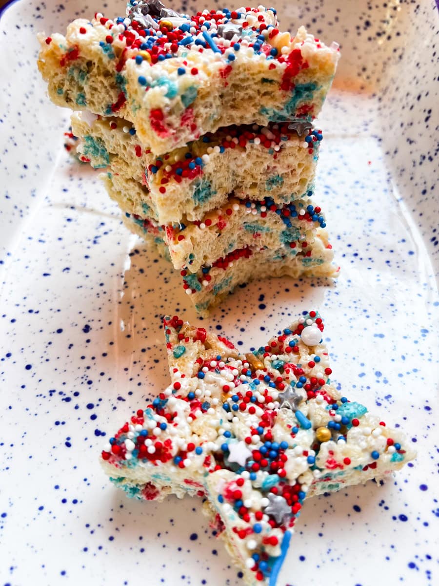 Star-shaped Fourth of July Rice Krispie treats decorated with red, white, and blue sprinkles stacked on a serving platter.
