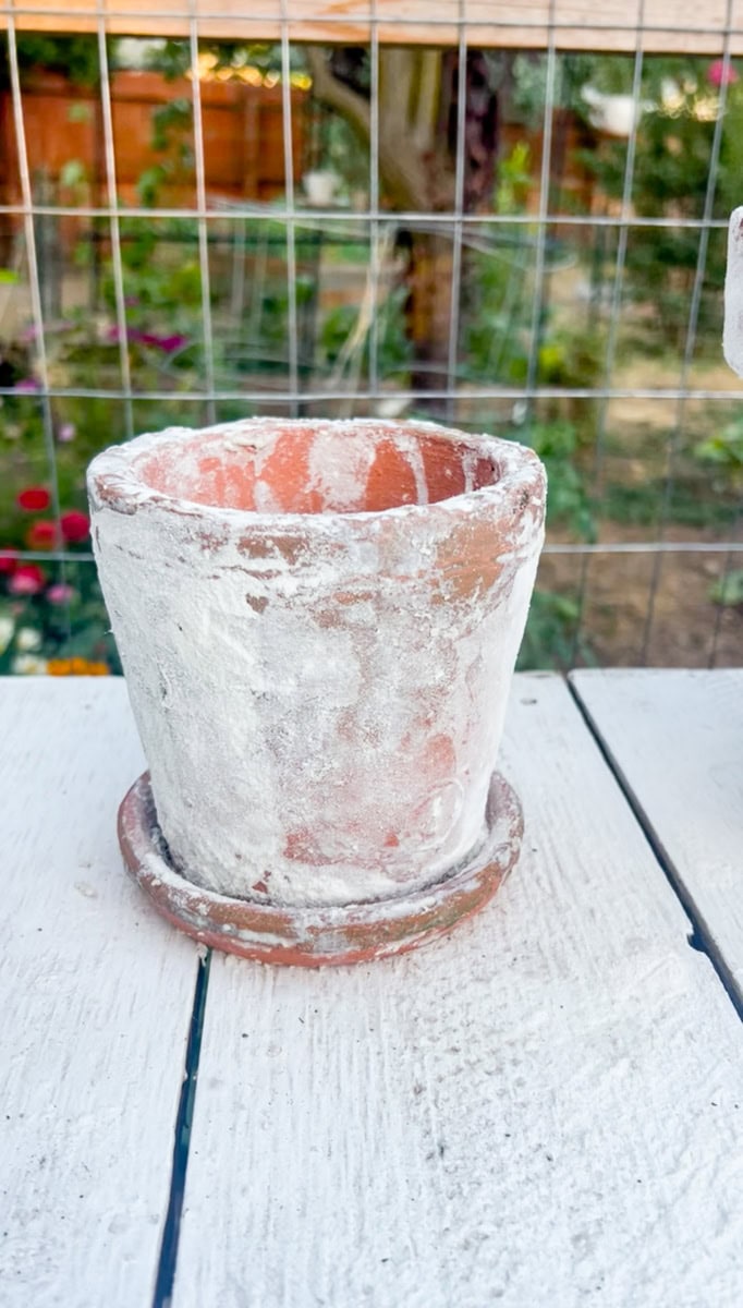 Finished aged terracotta pots with a faux white patina sitting on a matching saucer outdoors after the aging technique has dried.