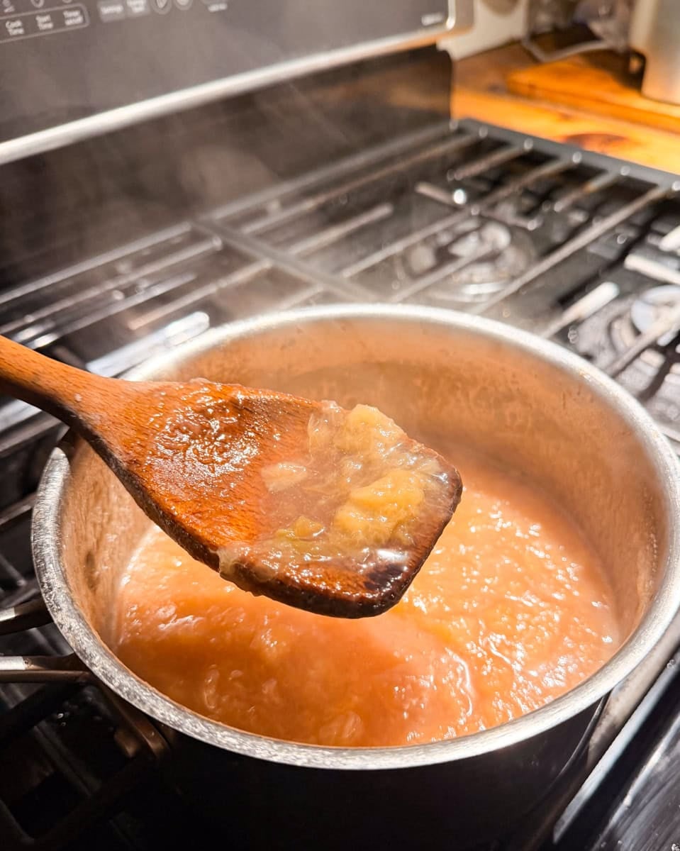 Wooden spoon lifting thick homemade peach jam from a saucepan as the no-pectin peach jam finishes cooking.