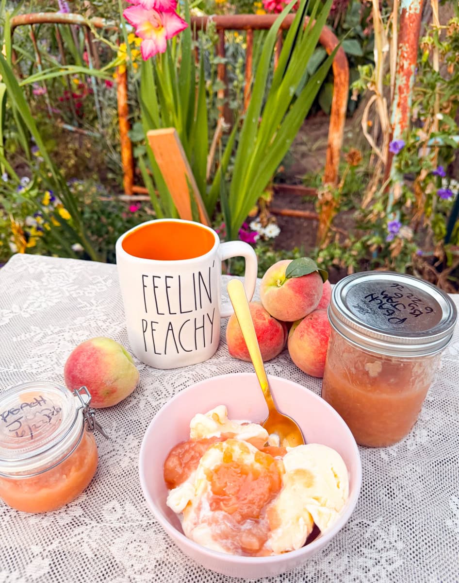 Homemade peach jam served over vanilla ice cream with fresh peaches and jars of peach jam on an outdoor garden table.