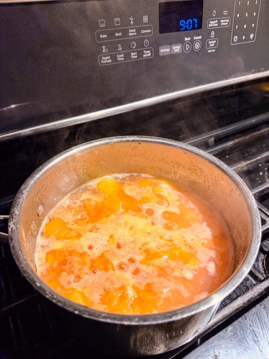 Peaches gently simmering in a saucepan as the fruit softens and releases its juices for peach jam.