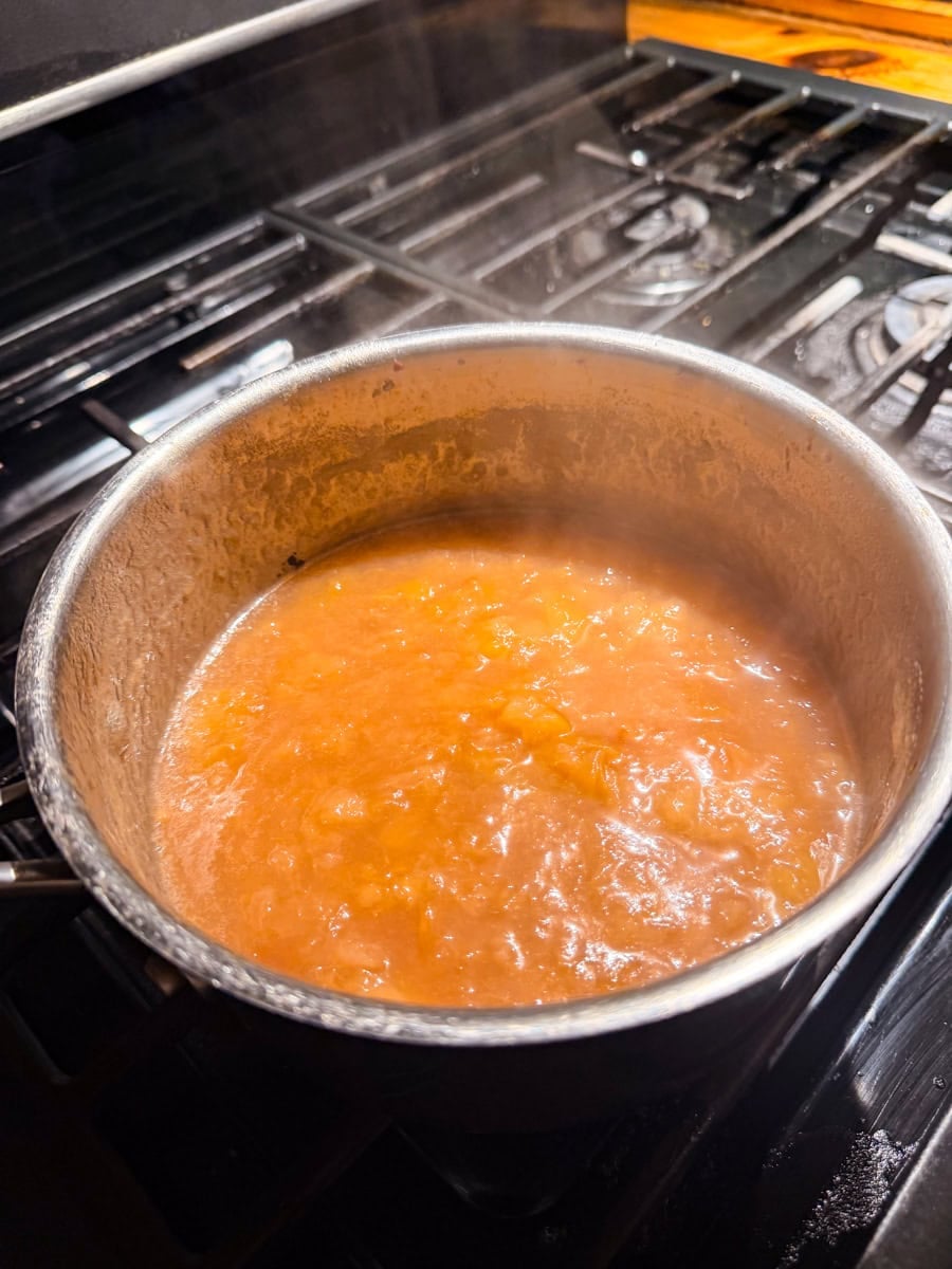 Peaches cooking in a saucepan as they soften and release their juices for fresh peach jam.