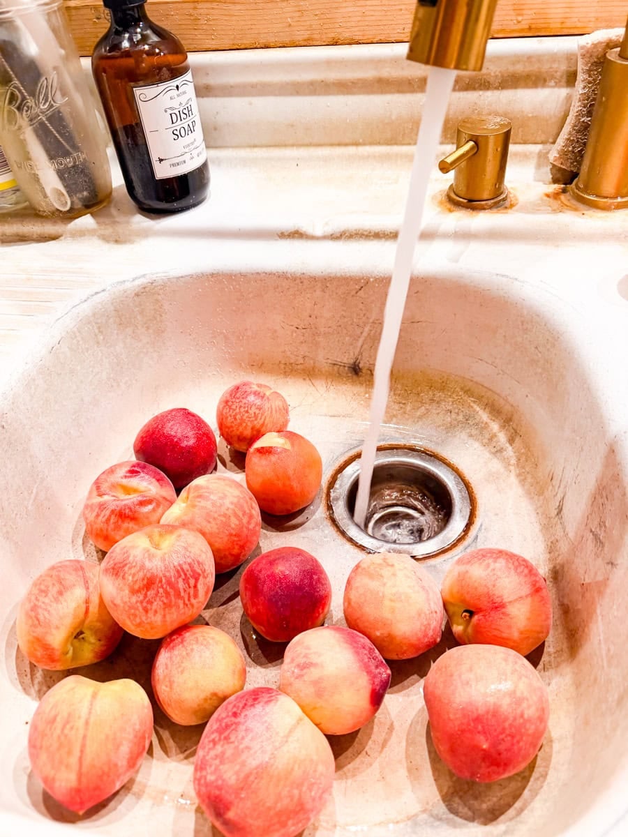 Fresh peaches being washed in a kitchen sink before making peach jam.