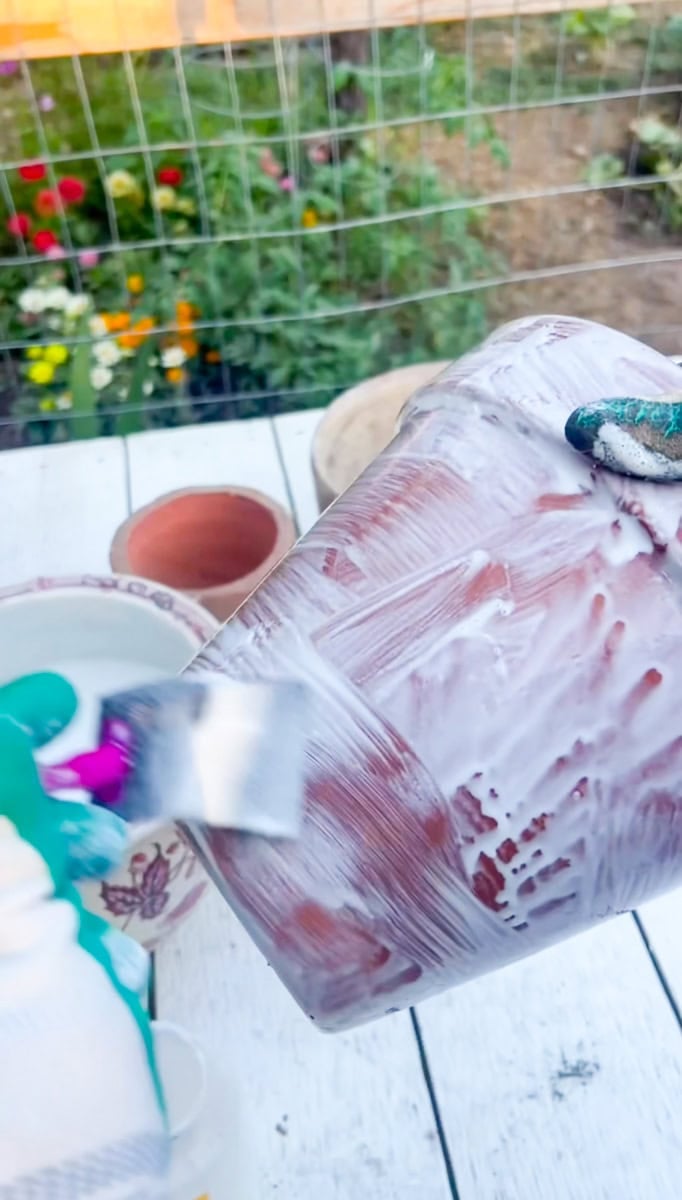 Wearing protective gloves while brushing a diluted Mod Podge mixture onto a clean terracotta pot to create a weathered finish.