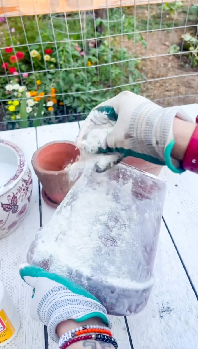 Wearing gloves while dusting flour over a wet Mod Podge-coated terracotta pot to create a realistic aged patina.