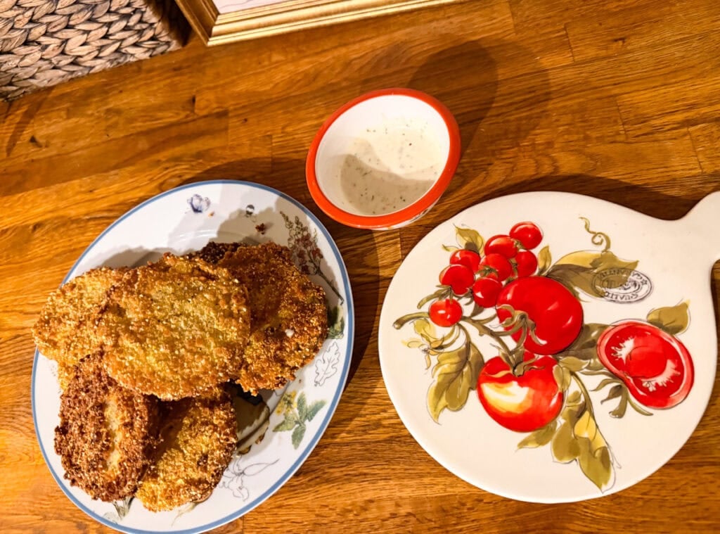 Plate of crispy fried green tomatoes served with ranch dipping sauce and fresh garden tomatoes.