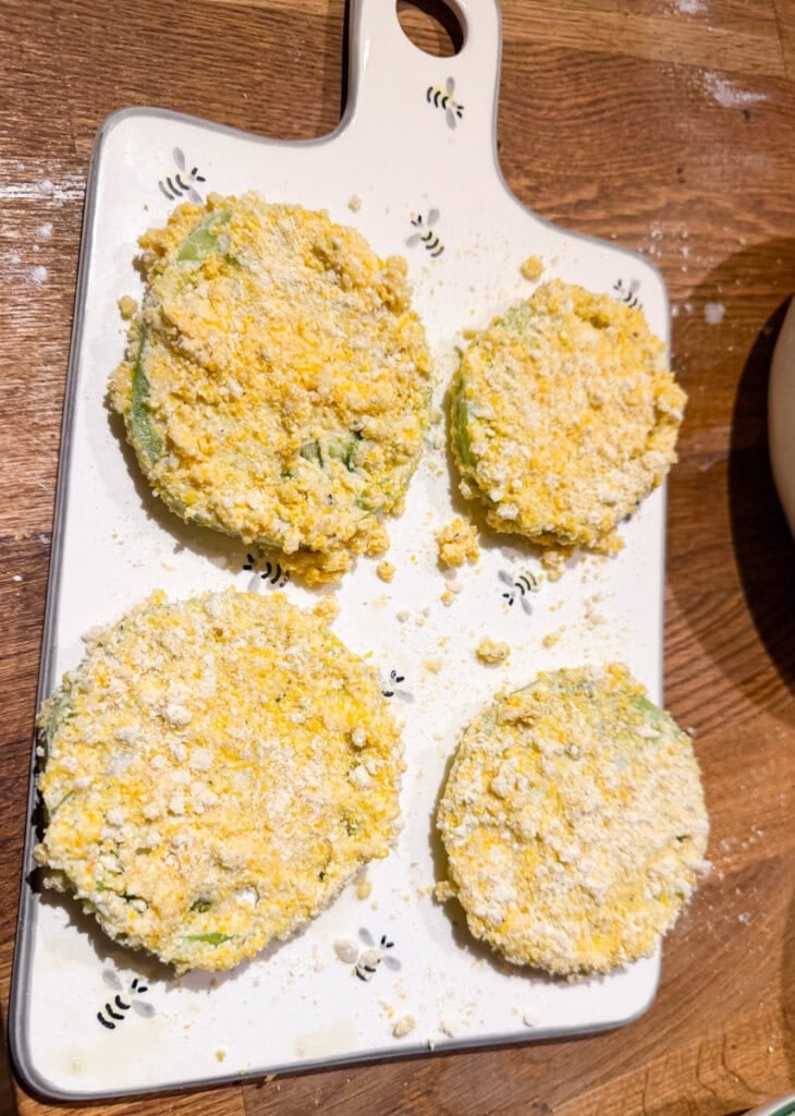 Green tomato slices coated in a crispy cornmeal and breadcrumb mixture and arranged on a cutting board.