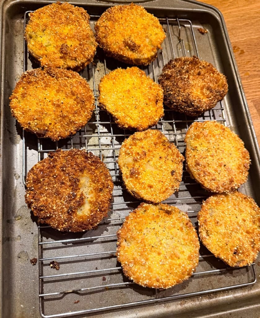 Crispy fried green tomato slices draining on a wire rack over a baking sheet.