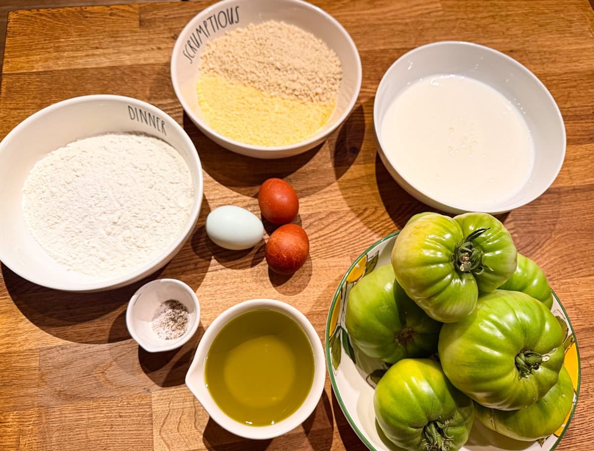 Ingredients for fried green tomatoes including green tomatoes, extra-virgin olive oil, sea salt, black pepper, eggs, flour, cornmeal, and breadcrumbs.