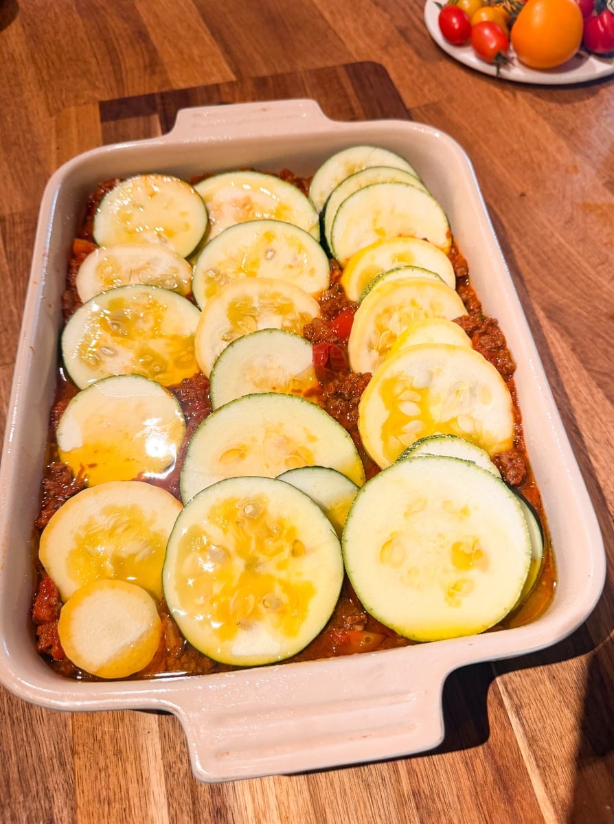 Sliced zucchini and yellow squash layered over the tomato mixture in a baking dish before adding the remaining vegetables.