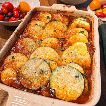 Freshly baked ratatouille topped with grated Parmesan cheese, featuring tender zucchini, yellow squash, tomatoes, and herbs in a casserole dish.