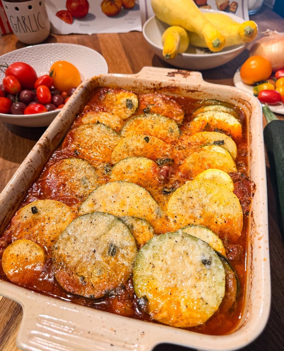 Freshly baked ratatouille topped with grated Parmesan cheese, featuring tender zucchini, yellow squash, tomatoes, and herbs in a casserole dish.