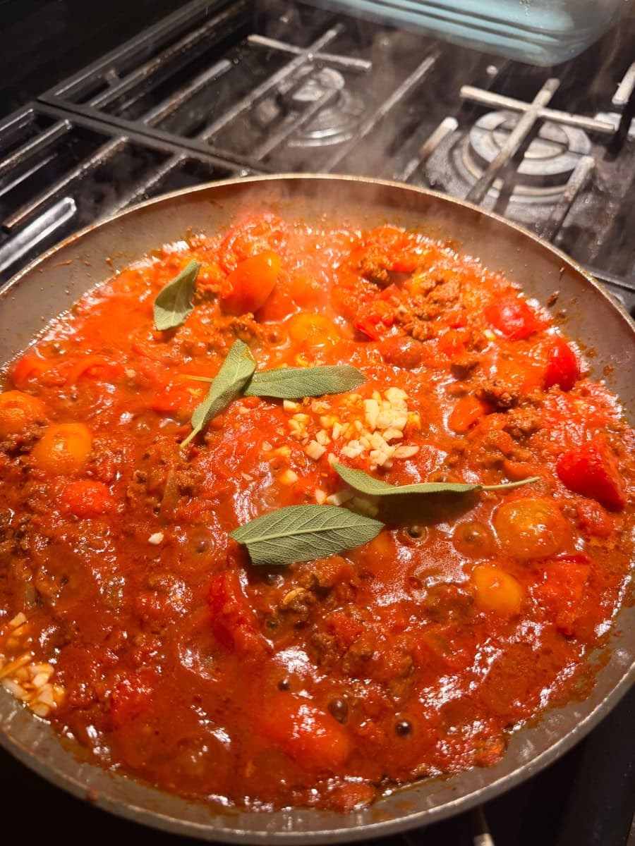 Homemade ratatouille sauce simmering in a skillet with tomatoes, garlic, fresh sage, marinara sauce, and ground beef.