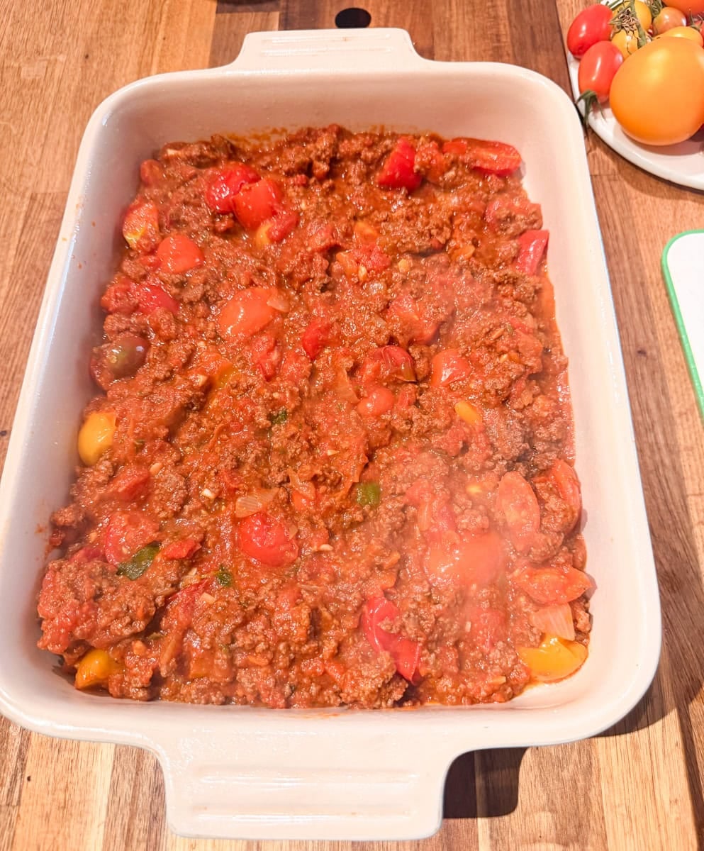 Homemade tomato and ground beef mixture spread evenly in a baking dish before adding the sliced vegetables.