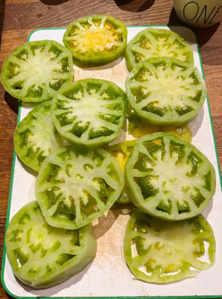 Sliced green tomatoes seasoned with sea salt and black pepper on a wooden cutting board.