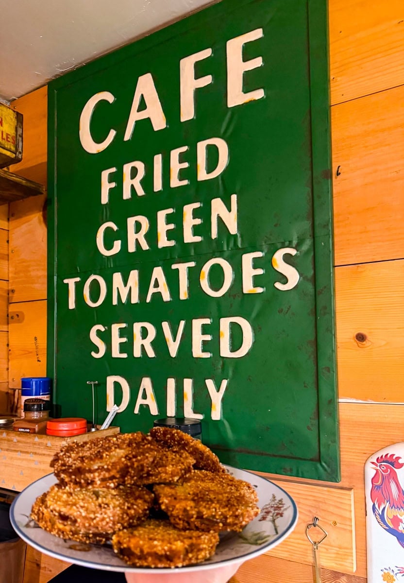 Plate of crispy fried green tomatoes displayed in front of a café sign reading “Fried Green Tomatoes Served Daily.”