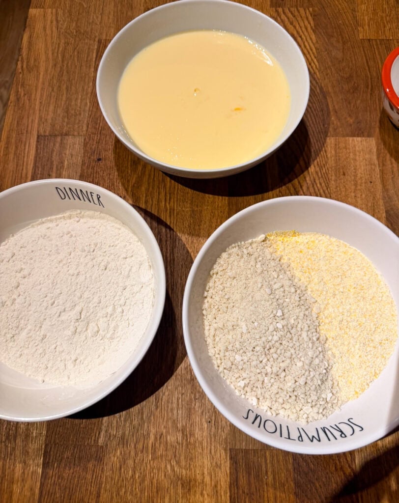 Bowls of beaten eggs, flour, and a cornmeal breadcrumb mixture for breading Southern-style fried green tomatoes.