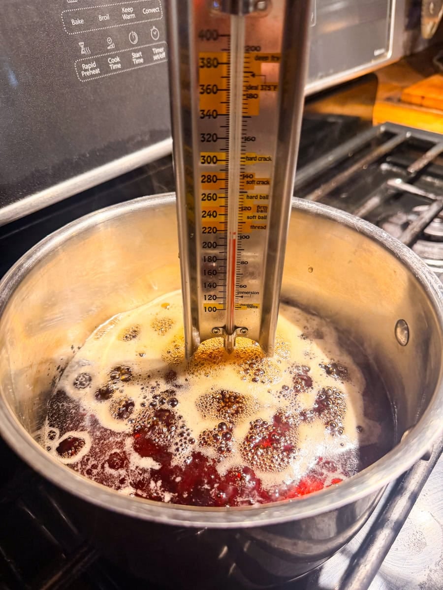 Pure maple syrup beginning to boil in a saucepan with a candy thermometer.