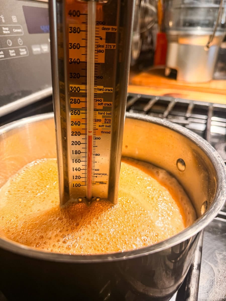 Pure maple syrup at a full rolling boil in a saucepan with a candy thermometer.