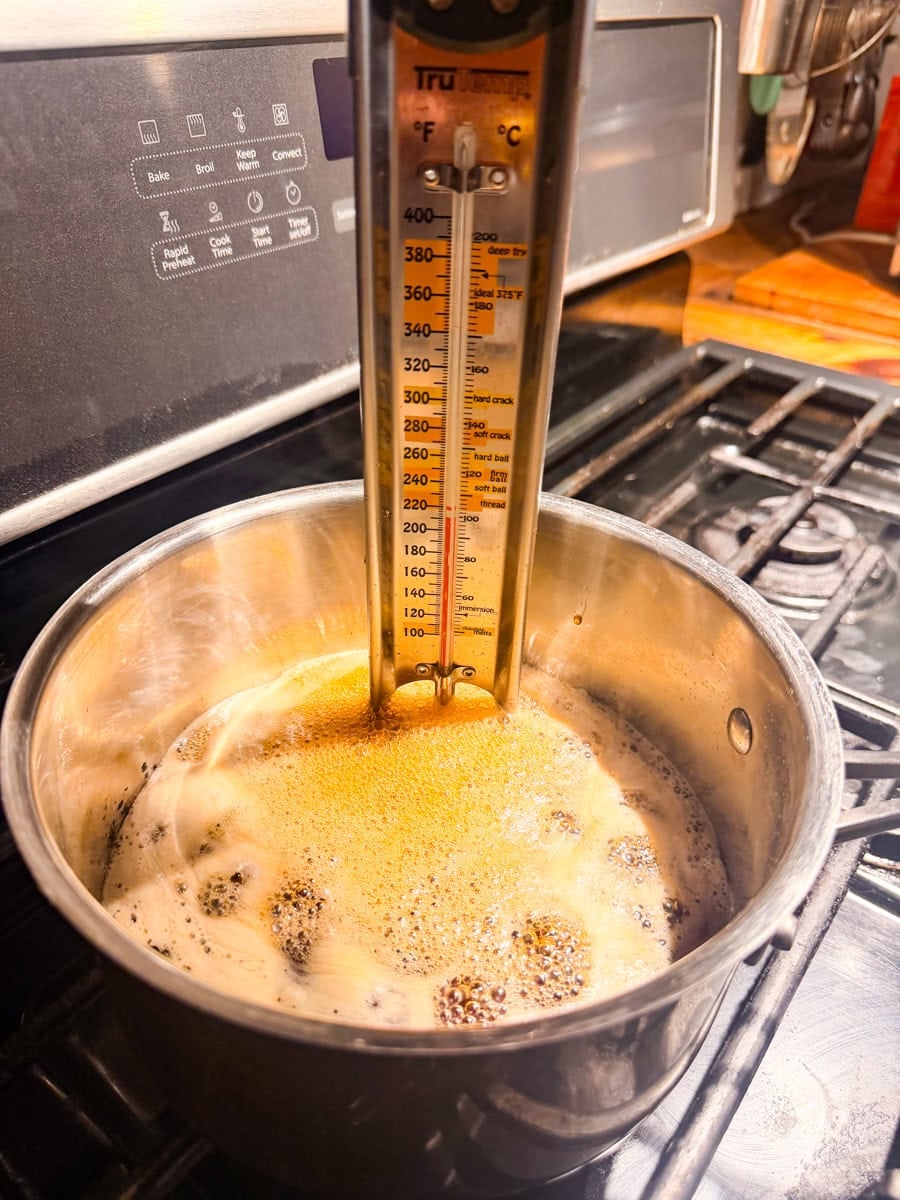 Pure maple syrup reaching a rolling boil in a saucepan with a candy thermometer.