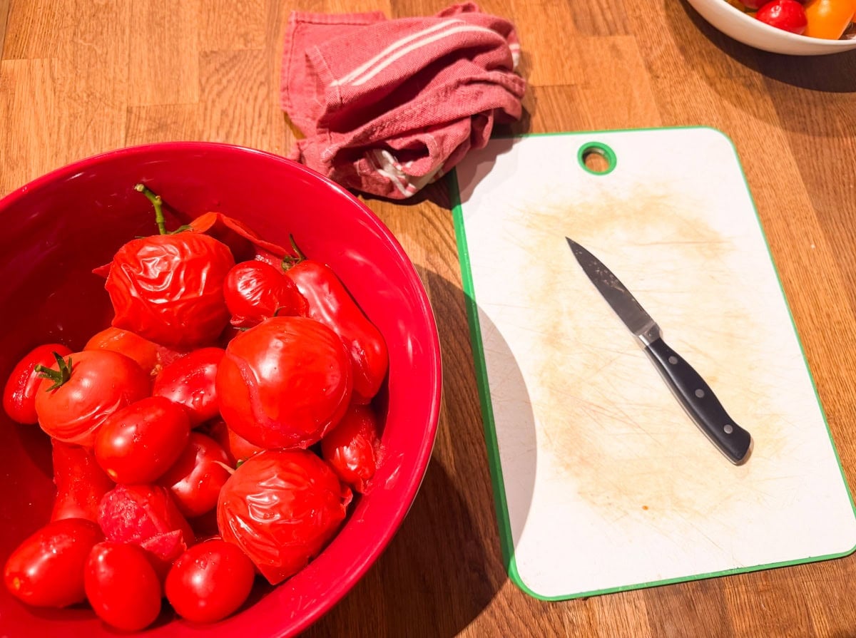 Bowl of peeled fresh tomatoes beside a cutting board and paring knife, ready to make Homemade Tomato Passata.