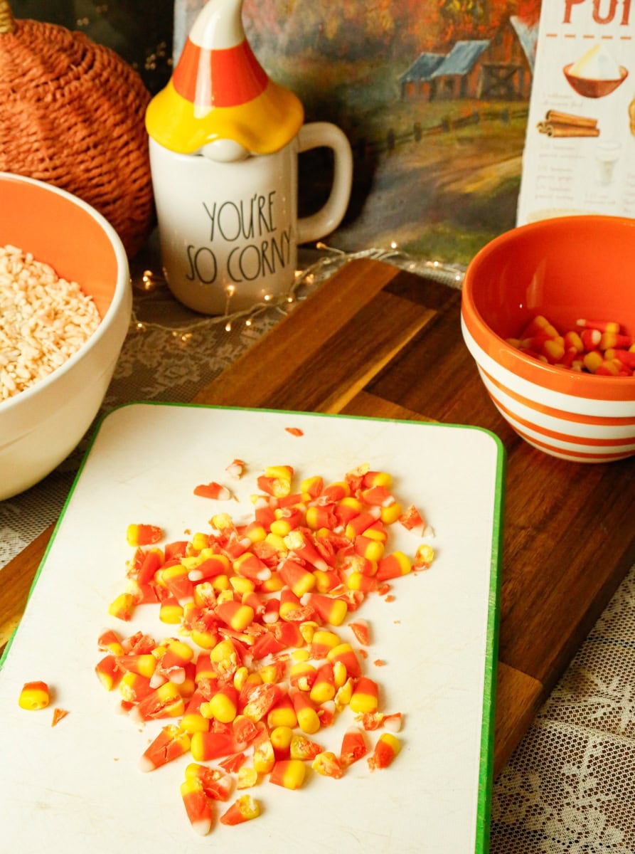Chopped orange, yellow, and white candy corn on a cutting board for homemade Halloween Rice Krispies Treats.