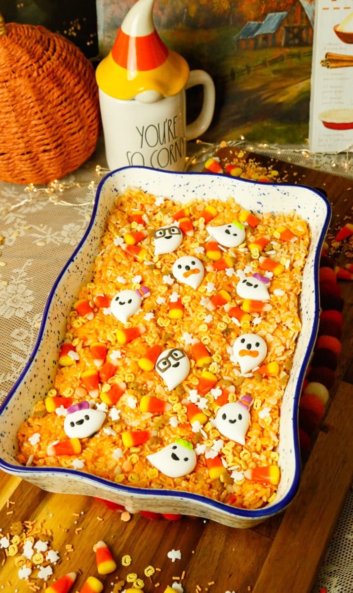 Decorating homemade Halloween Rice Krispies Treats with colorful candy corn, festive Halloween sprinkles, and adorable ghost-shaped candies.