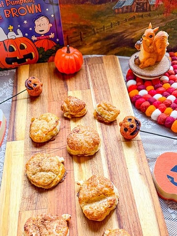 Pumpkin-shaped hand pies on a wooden board with Halloween decorations.