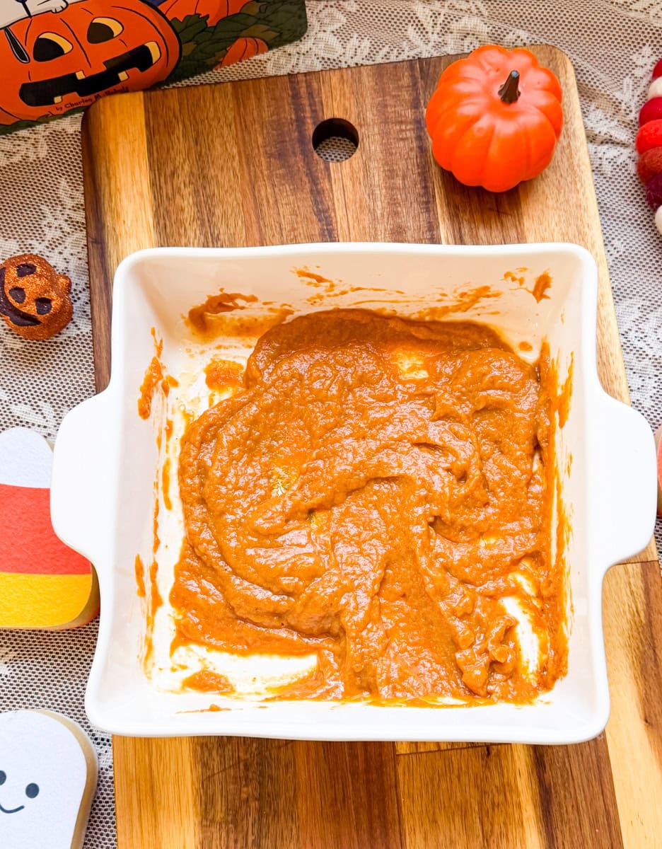 Homemade pumpkin pie filling mixed with brown sugar and pumpkin spice in a white baking dish, ready for filling puff pastry hand pies.