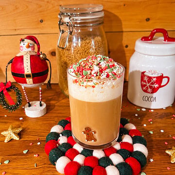 Homemade sugar cookie latte topped with whipped cream and festive Christmas sprinkles in a glass mug with a gingerbread man.