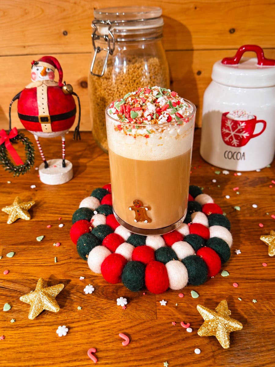  Homemade sugar cookie latte topped with whipped cream and festive Christmas sprinkles in a glass mug with a gingerbread man.