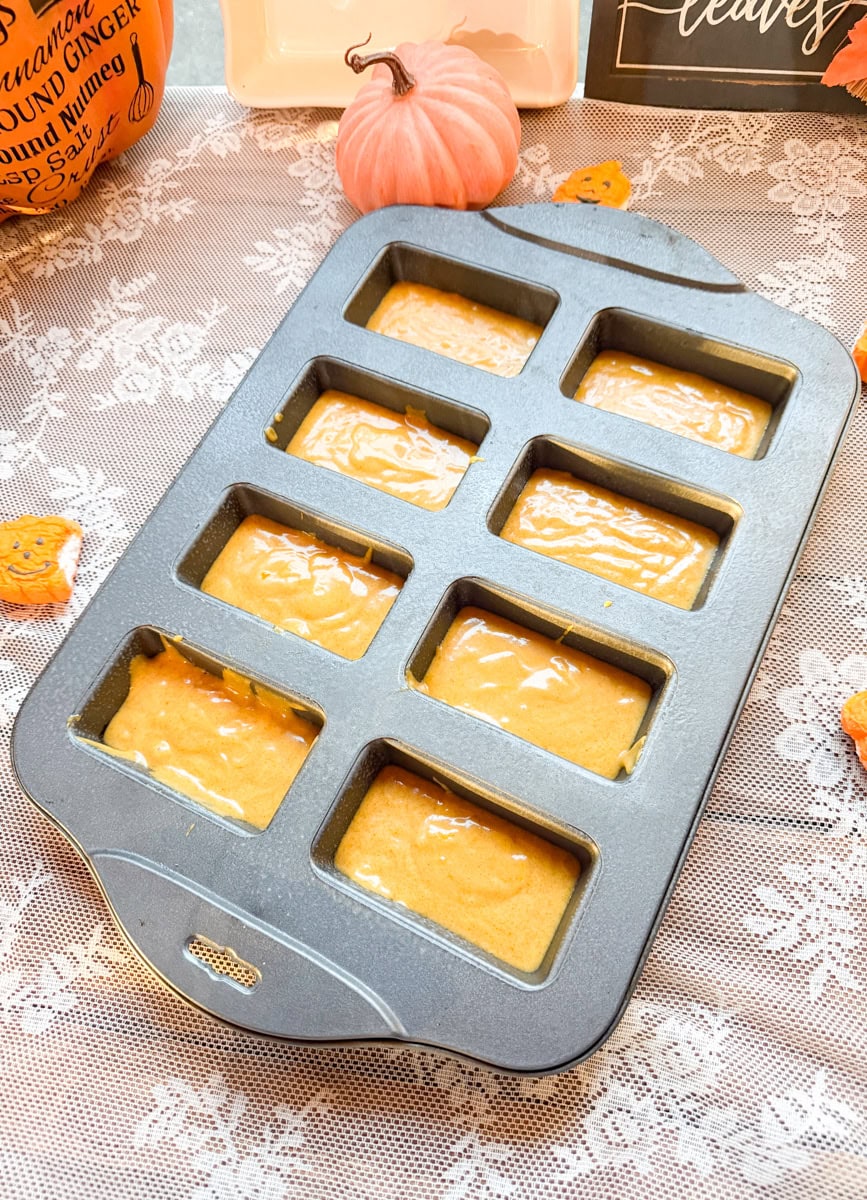 Eight individual cavities of a mini loaf baking pan filled with pumpkin bread batter and ready to bake.
