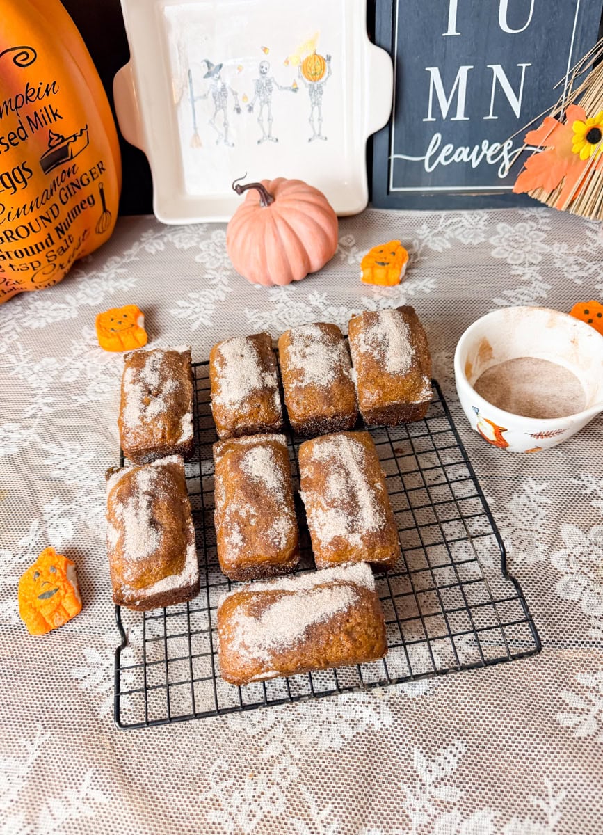 Seven golden mini pumpkin bread loaves topped with cinnamon sugar and arranged on a wire cooling rack.