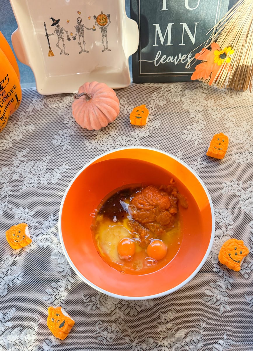 Overhead view of pumpkin puree, eggs, and wet ingredients in an orange mixing bowl for homemade mini pumpkin bread loaves.