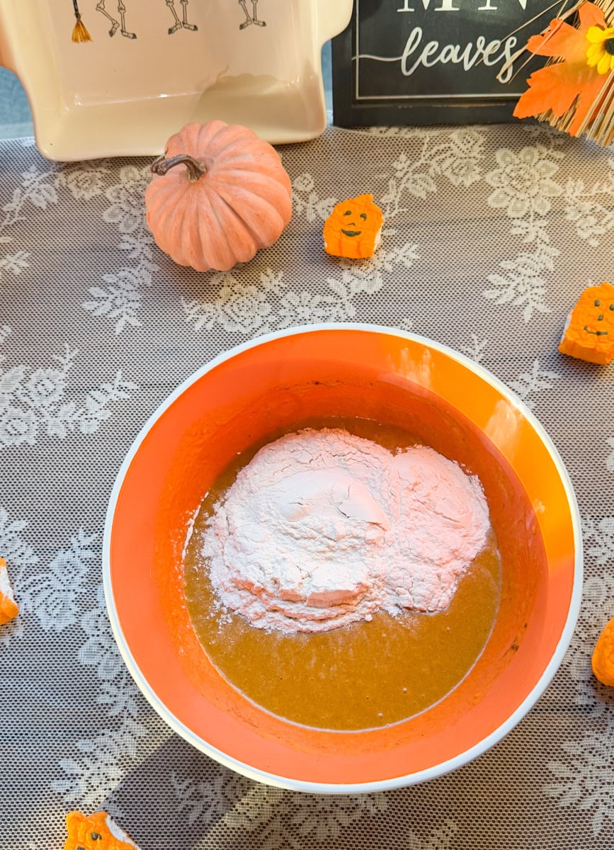 Flour added to a bowl of pumpkin bread wet ingredients before mixing the batter for mini pumpkin loaves.