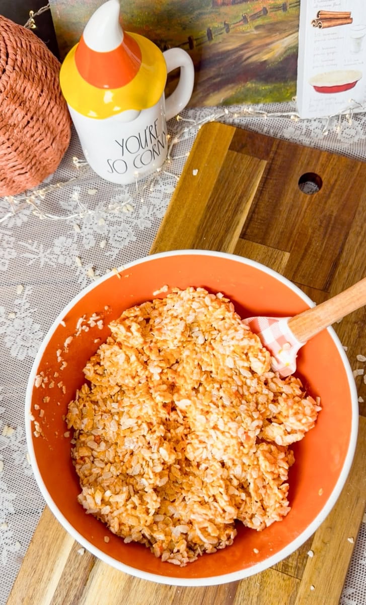 Candy corn Rice Krispies mixture transferred into a prepared baking dish, ready to be pressed into an even layer for Halloween treats.