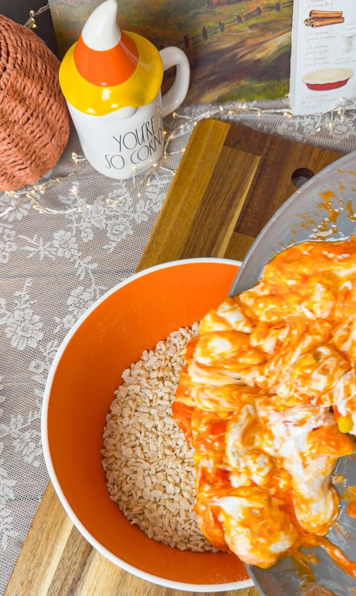 Melted candy corn marshmallow mixture poured over crispy rice cereal in a large mixing bowl to make gooey Halloween Rice Krispies Treats.