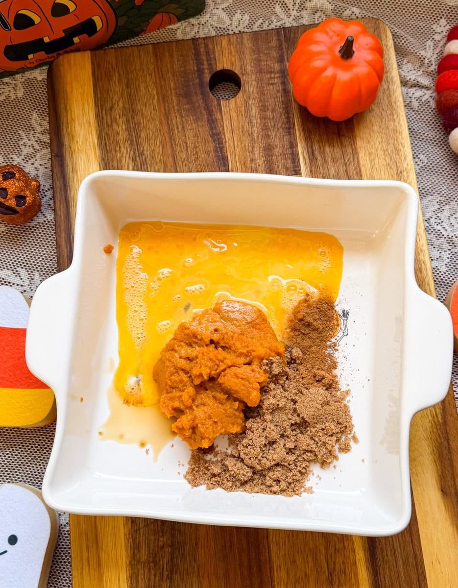 Pumpkin puree, brown sugar, and other pumpkin pie filling ingredients arranged in a white square baking dish before mixing.