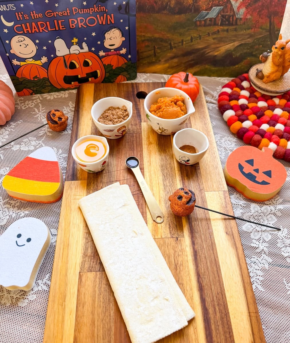 Ingredients for homemade pumpkin pie hand pies, including puff pastry, pumpkin puree, brown sugar, and spices, arranged with festive Halloween decorations.