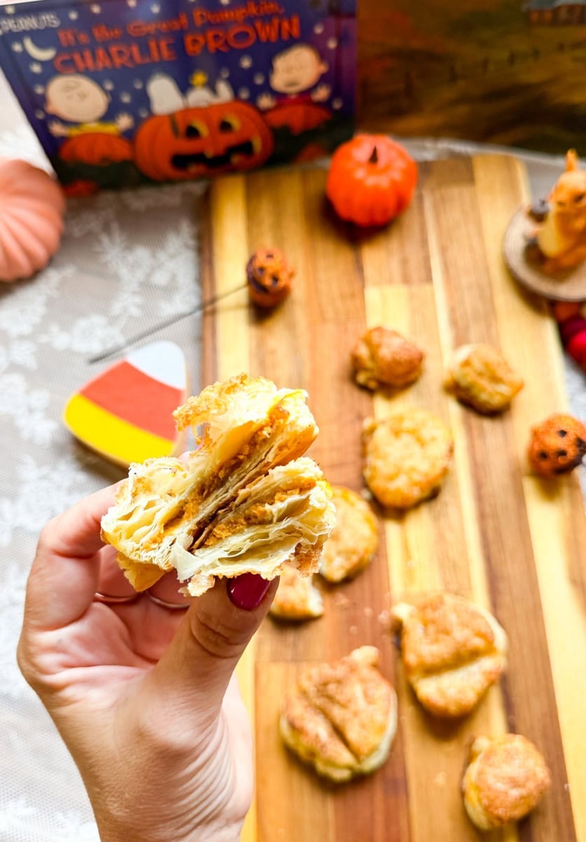 A freshly baked pumpkin pie hand pie broken open by hand to reveal sweet pumpkin filling and flaky layers of golden puff pastry.