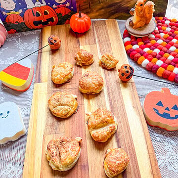 Golden brown pumpkin pie hand pies made with flaky puff pastry, arranged on a wooden cutting board with festive Halloween decorations, candy corn accents, and a Charlie Brown Great Pumpkin book.