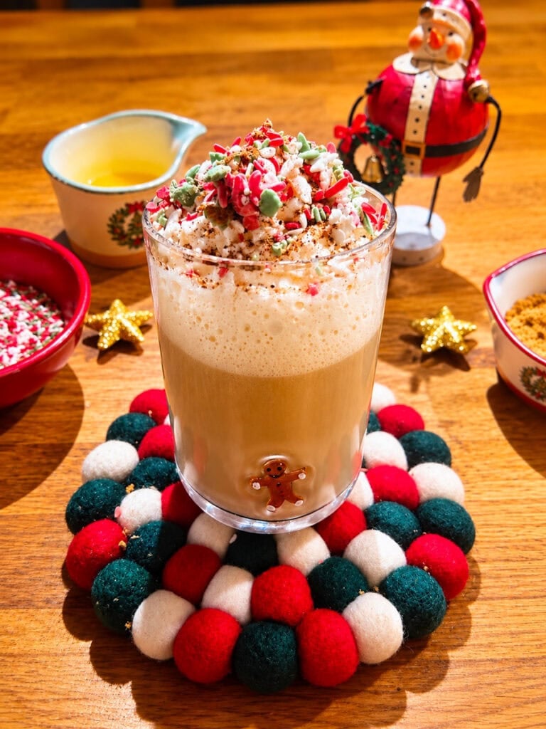 Homemade sugar cookie latte topped with whipped cream and Christmas sprinkles in a gingerbread glass mug.